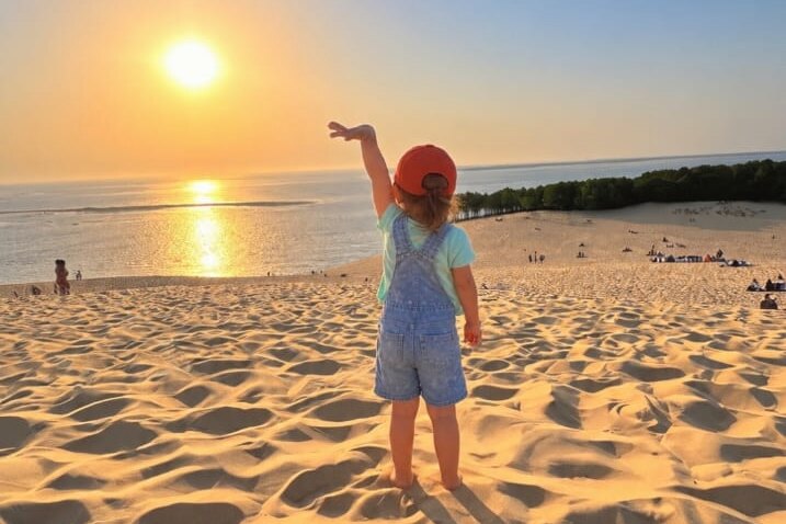 A child greets the setting sun on a dune by the ocean